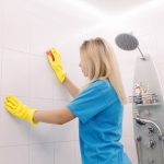 donna che pulisce doccia con spugna e guanti